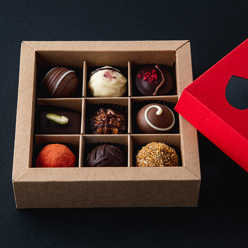 Offene Geschenkbox mit 16 bunten handgemachten Pralinen, roter Herzdeckel daneben – liebevolles Schokoladenpräsent.