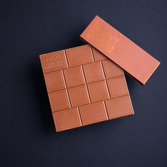 
                  
                    Vollmilch Tafel  auf dunklem Hintergrund und braune Banderole mit Herget Schokoladen-Logo
                  
                
