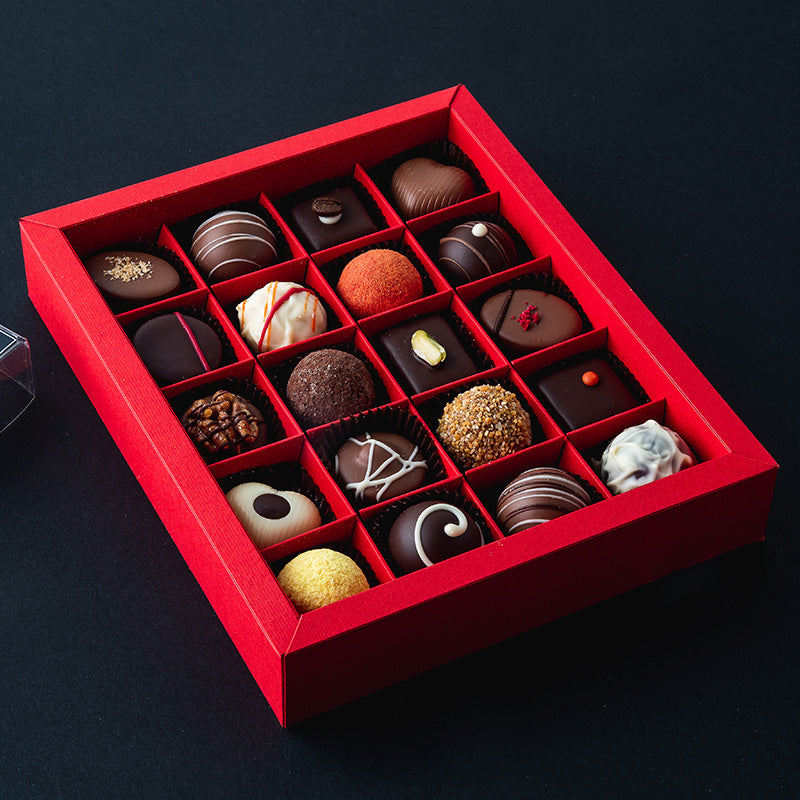 Pralinenpackung in rot mit 20 unterschiedlichen Pralinen und Trüffeln auf dunklem Hintergrund. Zum Beispiel Espressomarzipan, Nougat und Kirsche. 