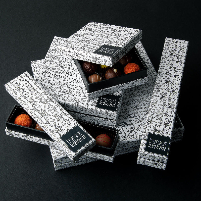 Handgemachte Pralinen in schwarz-weißer Geschenkbox mit Muster, stilvoll gestapelt – edle Schokoladengeschenkverpackung der Herget Schokoladenmanufaktur.
